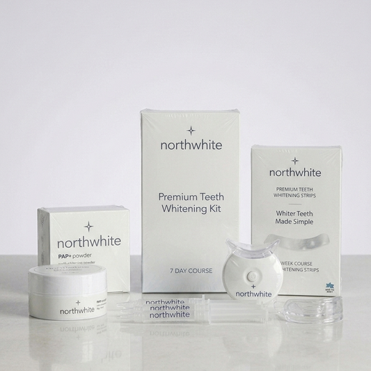 Northwhite Premium Teeth Whitening Kit displayed with its white packaging boxes, a small jar of powder, and a clear handheld device on a light gray reflective surface.